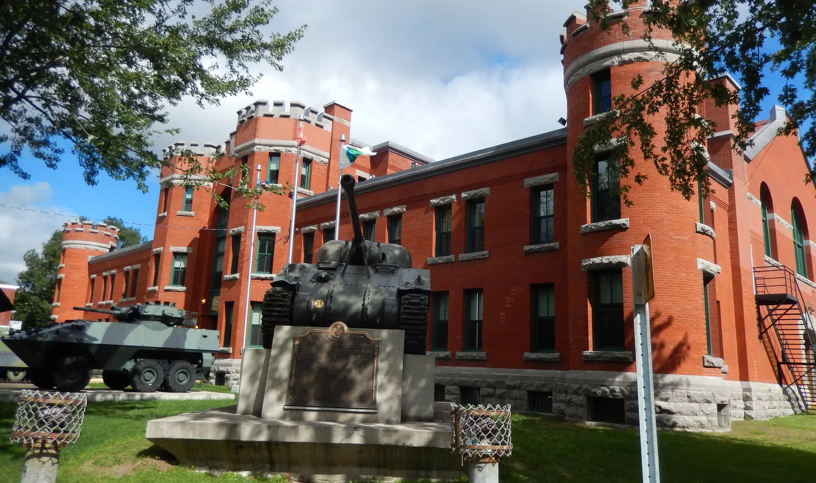 La façade de brique rouge du manège militaire, avec ses tours crénelées, et le char Sherman « Cathy » devant l’entrée.